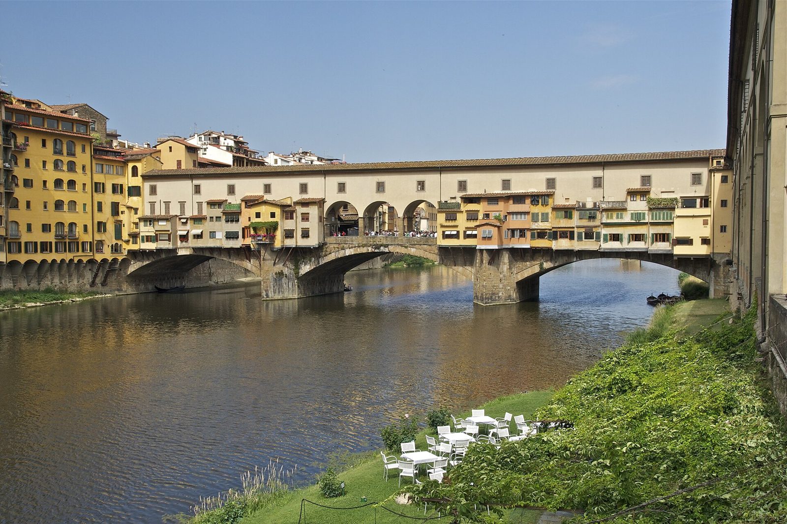 Il Ponte Vecchio sull'Arno in una giornata di sole, con le botteghe colorate a sbalzo sull'acqua e il corridoio sopraelevato che corre sopra di esse