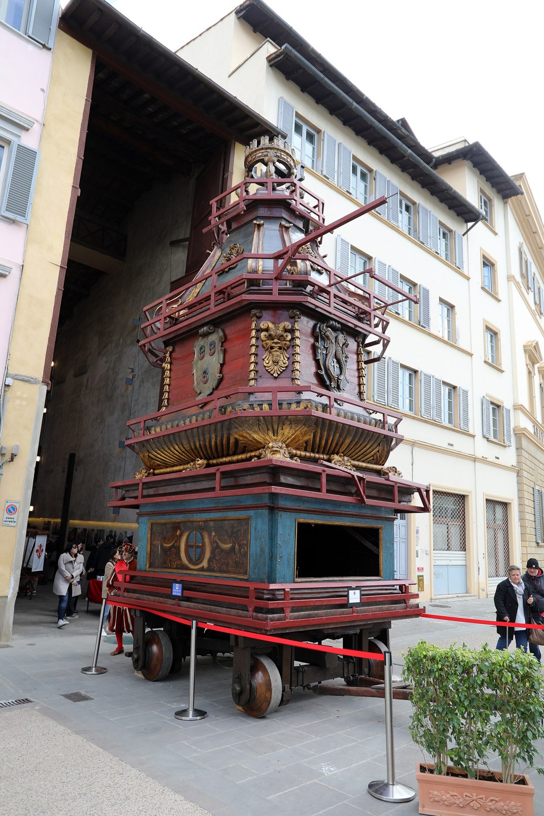 Il Brindellone, alto carro di legno dipinto di rosso e azzurro con dorature, stemmi e una corona in cima, fermo in strada davanti al suo deposito, delimitato da un nastro rosso